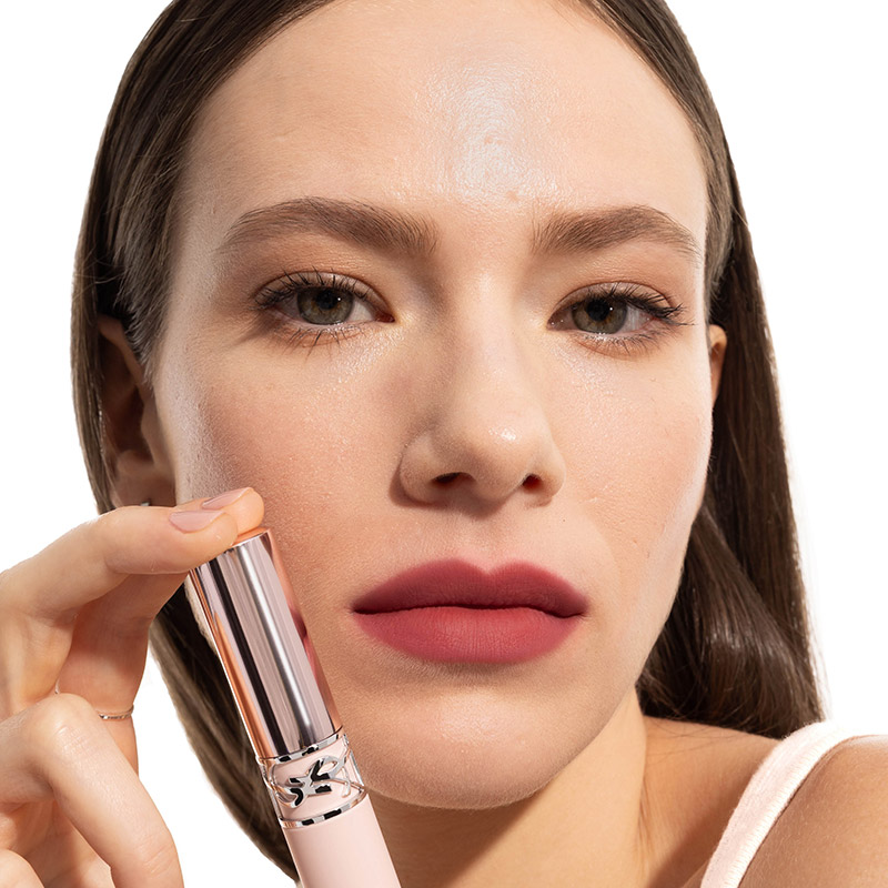 Una modella con labbra rosse opache tiene un tubetto di rossetto YSL vicino al viso.
