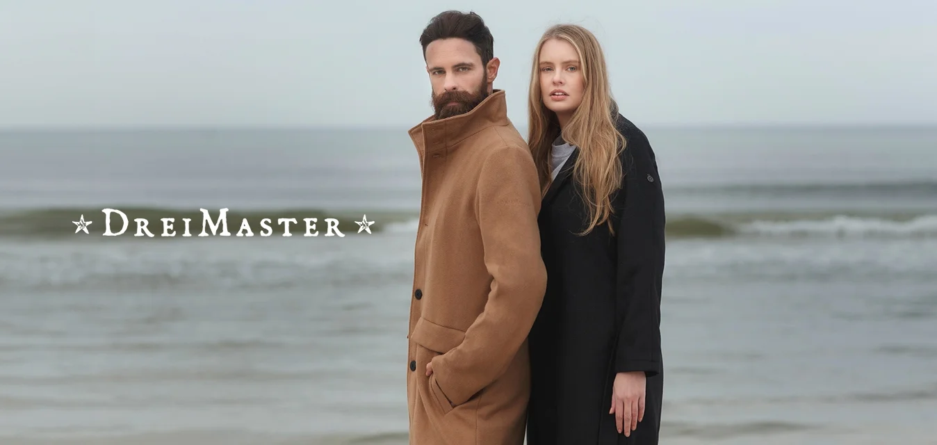 Cappotto di lana marrone con colletto alto e chiusura a bottoni; cappotto nero con maniche lunghe e tasche. Entrambi sono indossati da modelli vicino al mare.