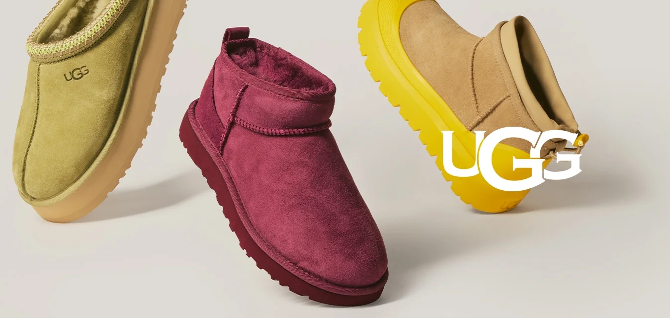 Tre paia di pantofole UGG in giallo-verde, rosso scuro e beige con suole gialle, esposte su uno sfondo neutro.