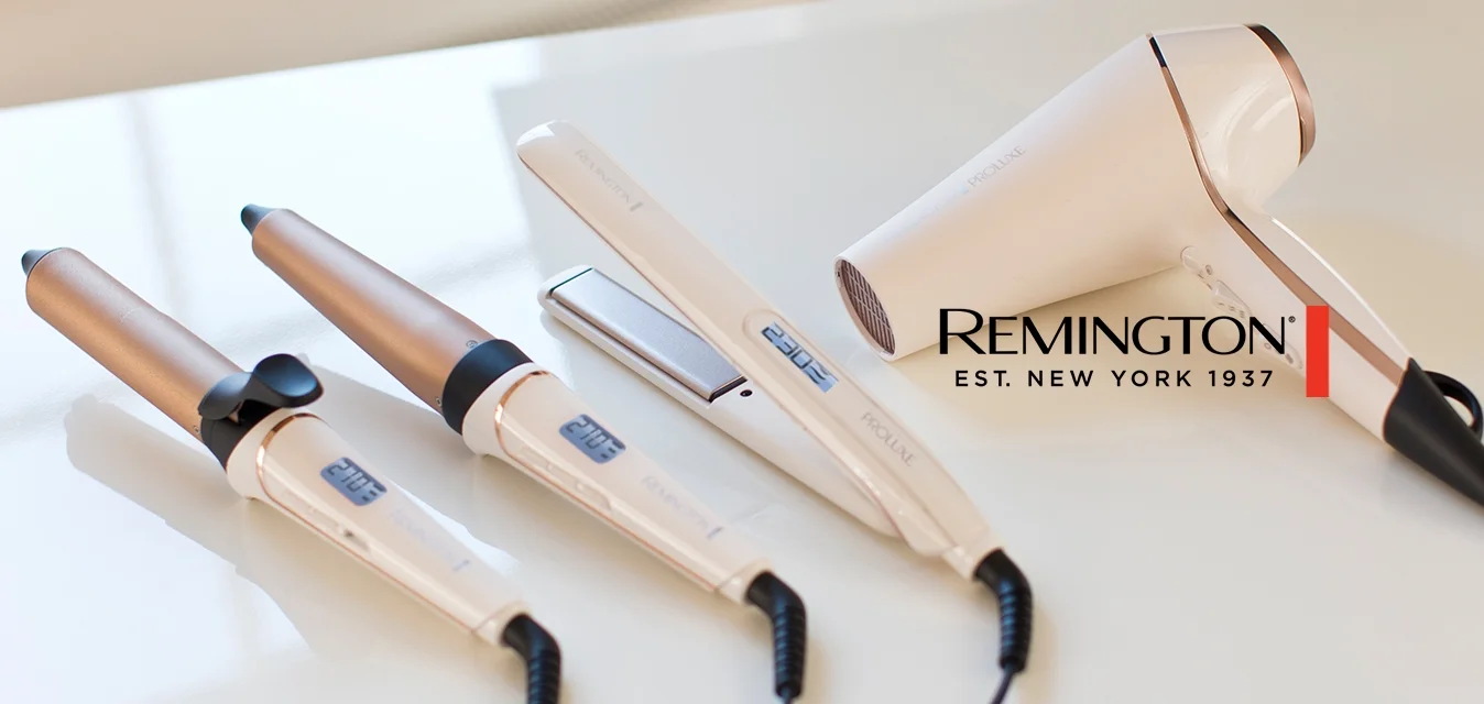 Due arricciacapelli, una piastra per capelli e un asciugacapelli, tutti bianchi con dettagli dorati, posizionati su un piano di lavoro bianco.