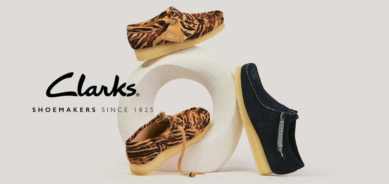 Due mocassini marroni con stampa a tigre e un mocassino blu navy con suola beige esposti su una base scultorea bianca.