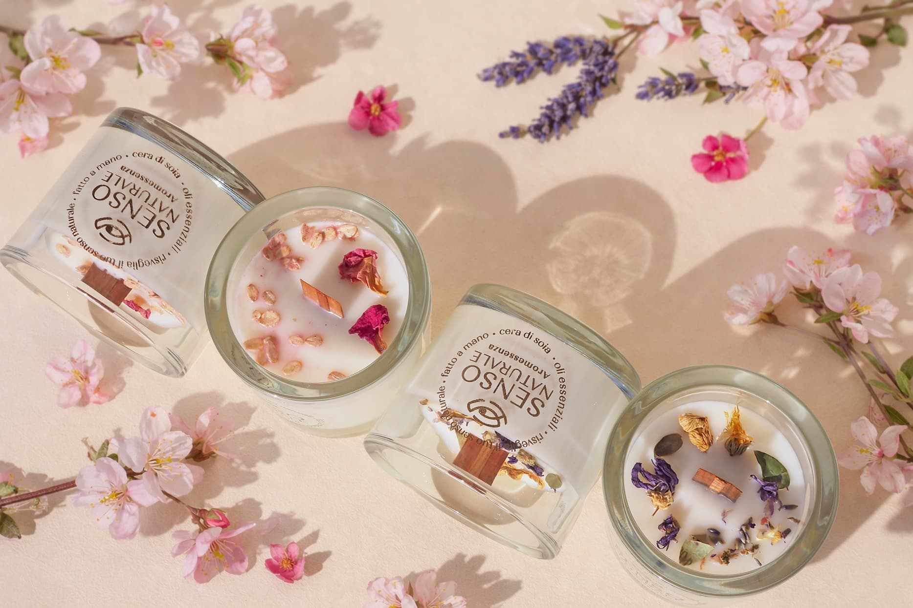 Four scented candles with dried flowers and petals scattered around them.