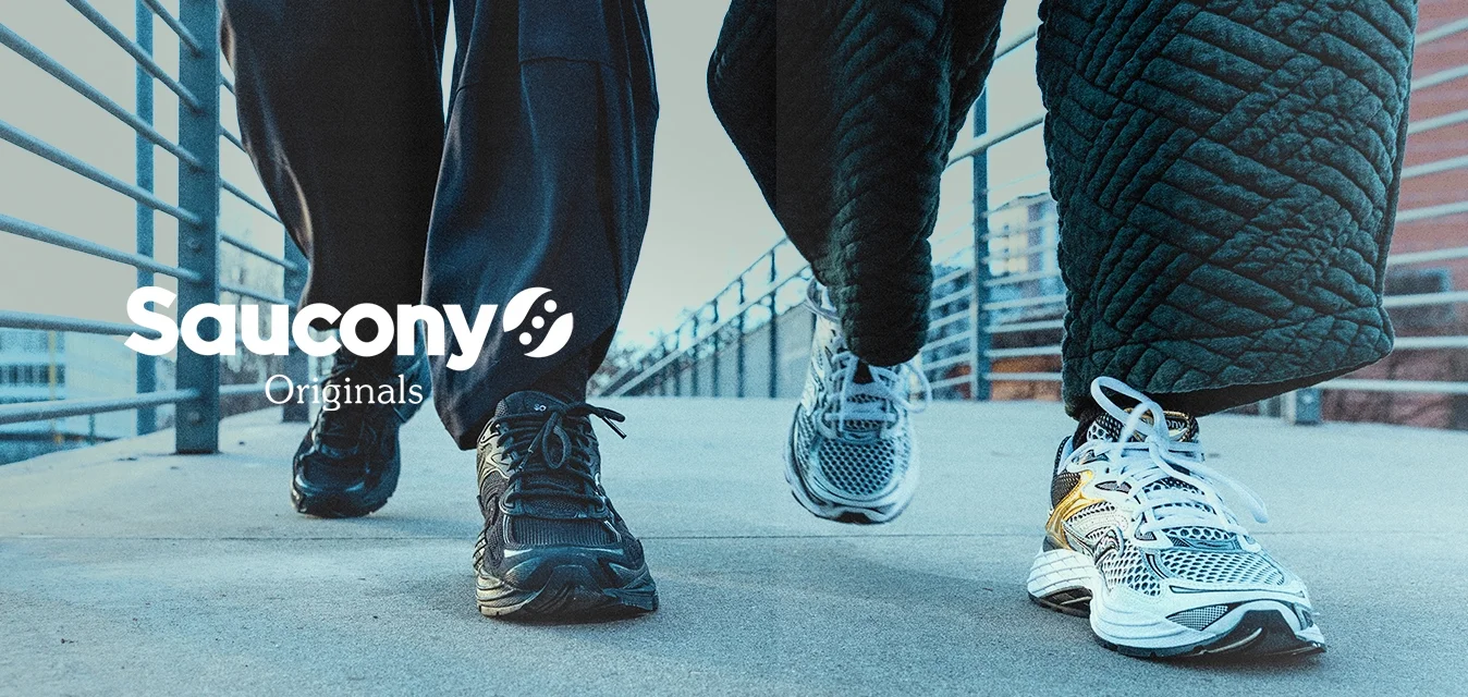 Due persone che camminano su un ponte all'aperto, indossando sneakers e abbigliamento scuro, con parapetti in metallo su entrambi i lati.