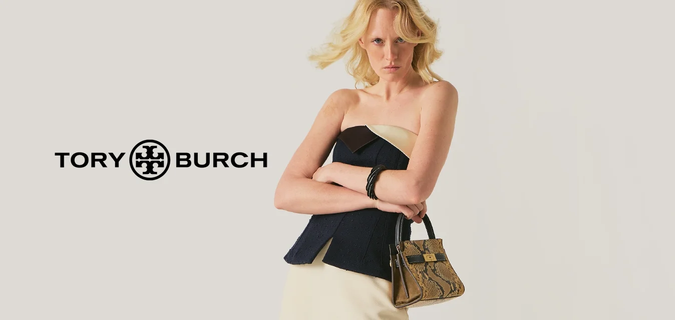 Donna con le braccia incrociate che indossa un vestito senza spalline nero e crema, tiene una borsa in pelle di serpente e indossa tacchi mule beige pelosi.