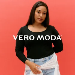 Donna con lunghi capelli scuri che indossa una maglia nera a maniche lunghe, jeans azzurri chiari e una camicia bianca annodata in vita, su uno sfondo corallo.