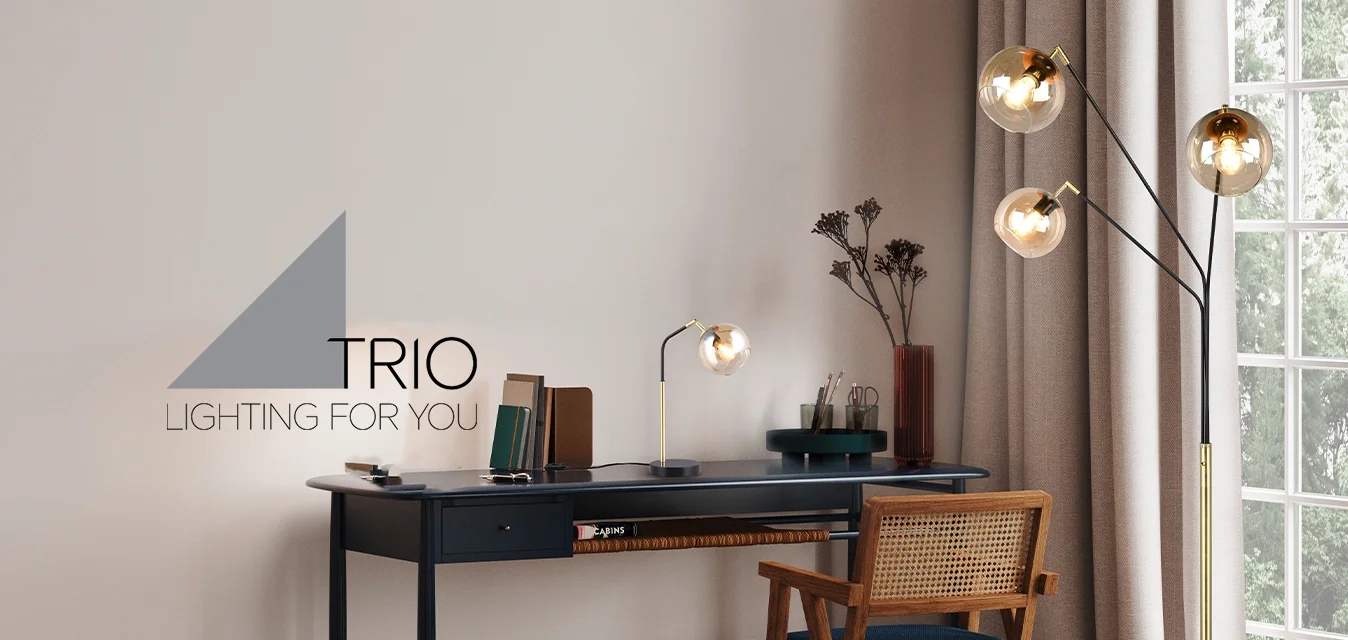 Spazio di lavoro moderno con scrivania scura, sedia di legno, lampada da tavolo, lampada da terra con tre bulbi, libri, piante essiccate e grande finestra con tende beige.