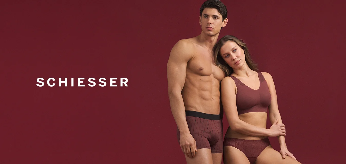 Costumi aderenti da uomo a righe nere e reggiseno sportivo e slip senza cuciture da donna color bordeaux, entrambi in tessuto morbido, su sfondo rosso scuro.