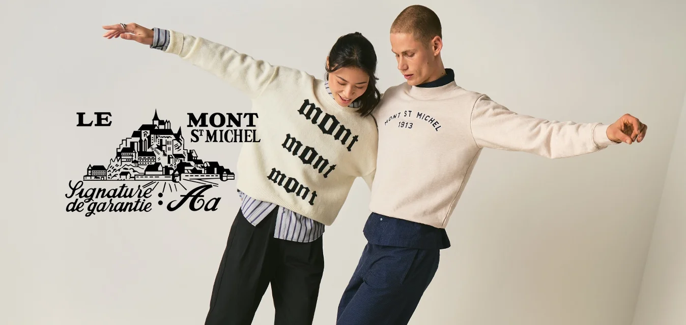 Due persone in equilibrio su una trave di legno all'interno, che indossano maglioni e pantaloni casual, con le braccia distese per mantenere l'equilibrio.