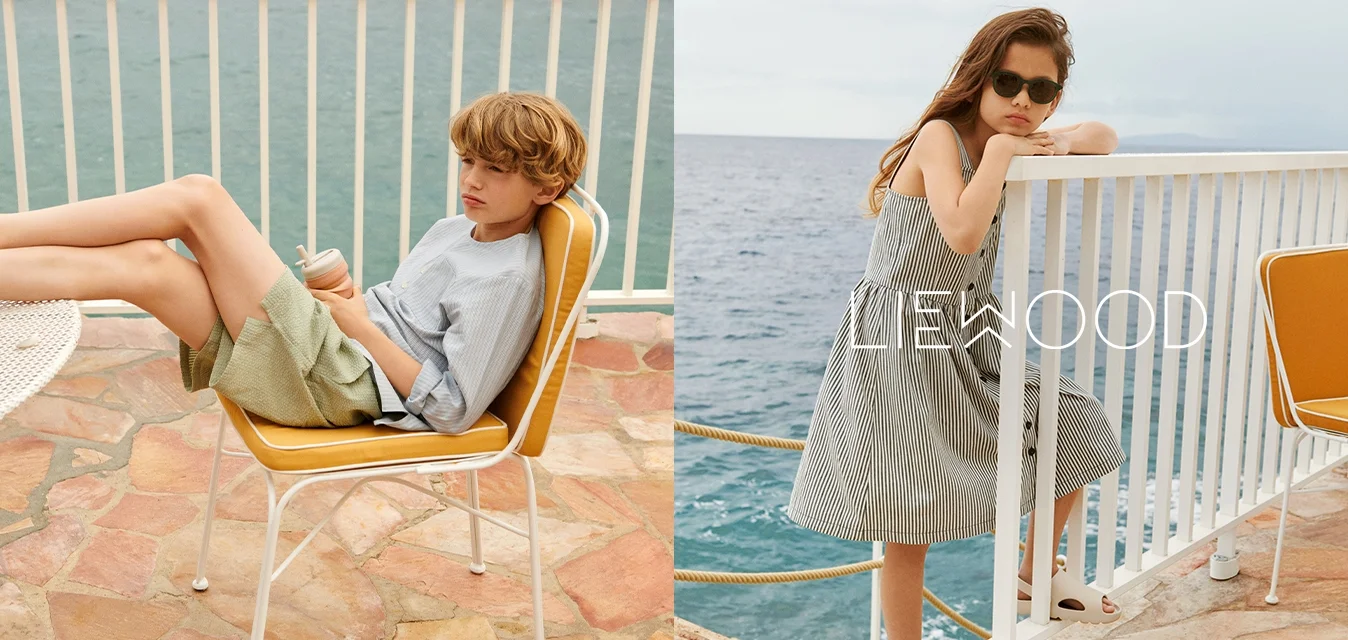 Maglietta a righe blu e pantaloni verdi su un bambino, vestito a righe su un altro. Entrambi in abbigliamento estivo casual, seduti vicino all'acqua.