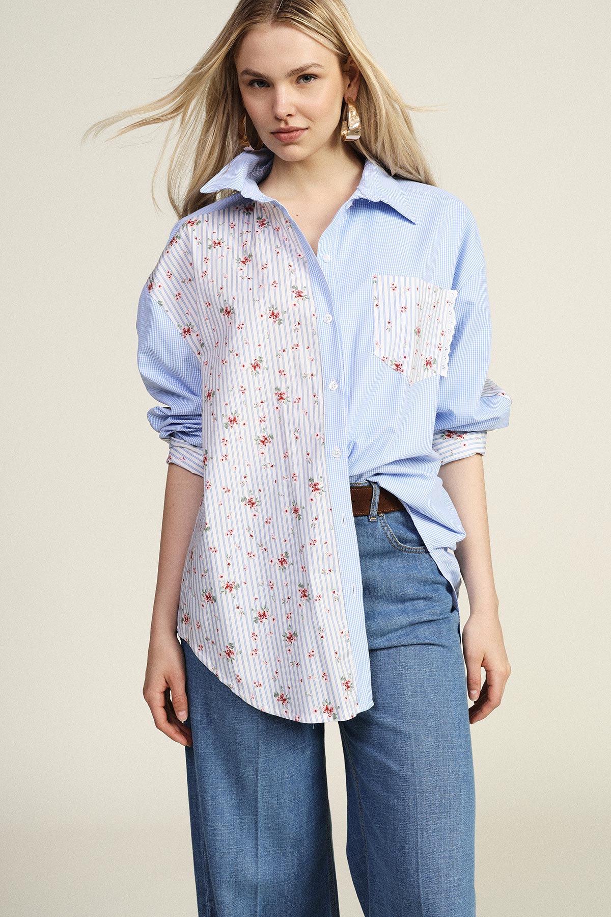 Woman modelling blue mixed-striped and floral oversized shirt tucked into wide-leg jeans on neutral background