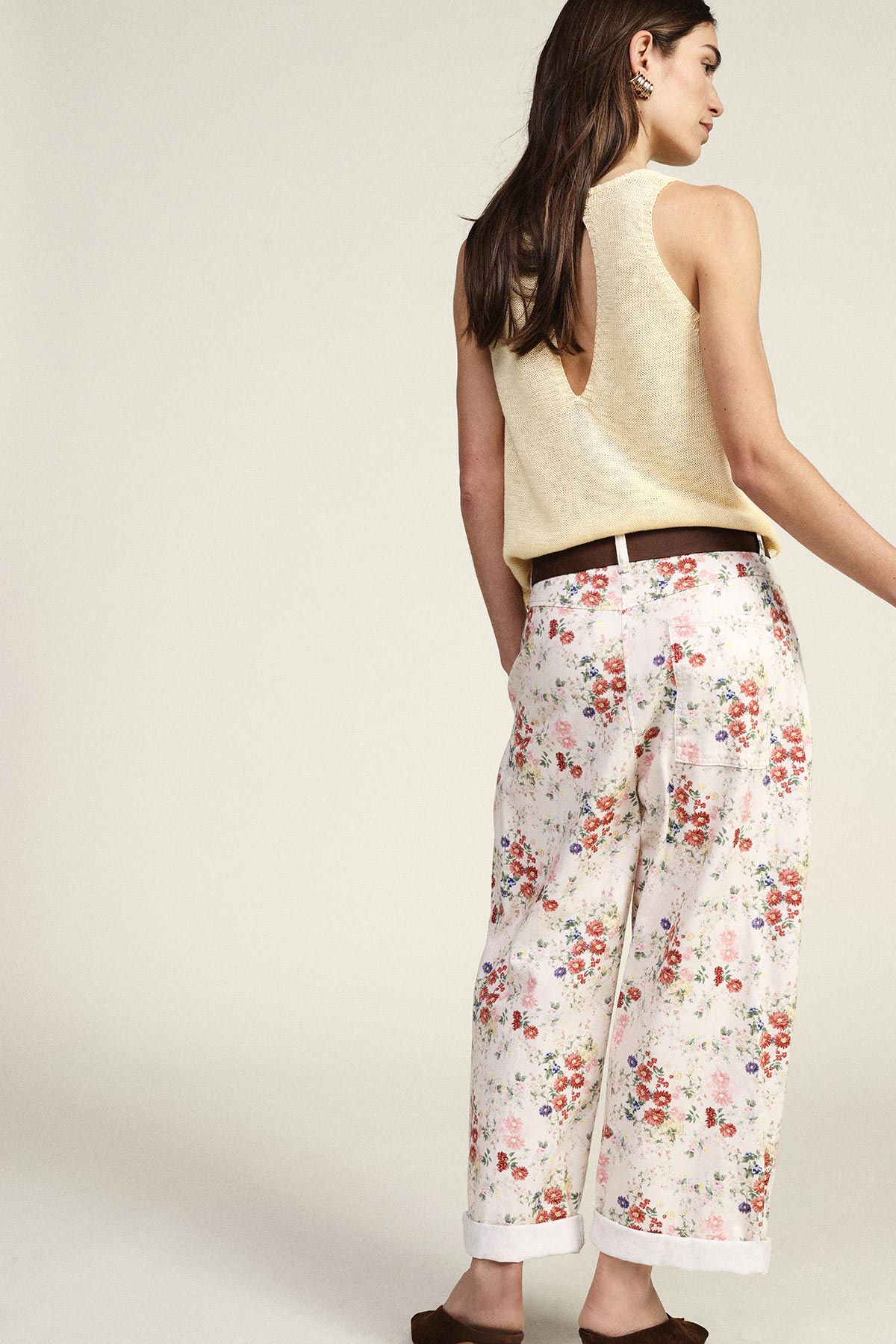 Woman from behind wearing a sleeveless beige knit top with a deep V back, floral wide-leg cropped trousers and a brown belt