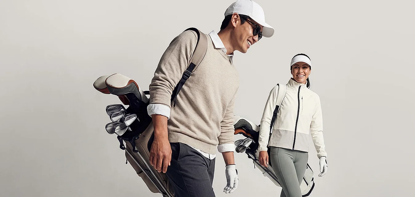 Uomo e donna che camminano portando borse da golf, vestiti con abbigliamento sportivo da golf e cappellini, su uno sfondo chiaro e uniforme.