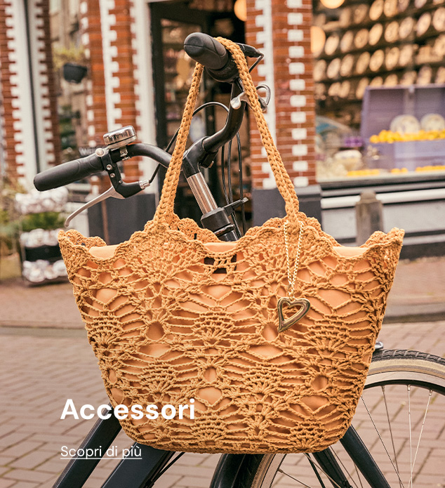 Crocheted tan tote bag with heart charm hanging on a bicycle handlebar in front of a city shop window