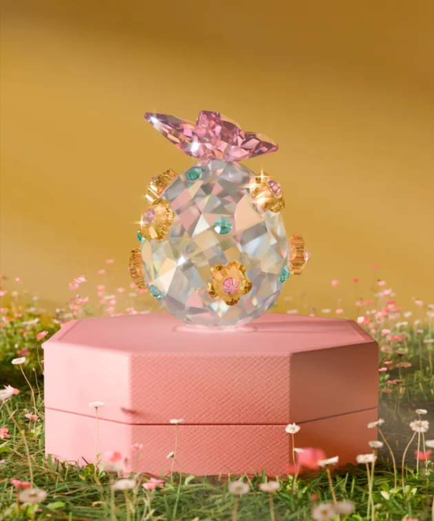 Uovo in cristallo Swarovski sfaccettato impreziosito con sfumature rosa, blu e oro e sormontato da una farfalla in cristallo Swarovski rosa.