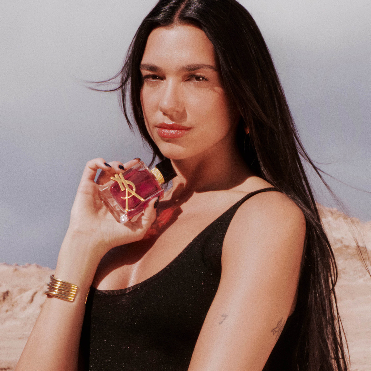Dua Lipa tiene un flacone di profumo YSL Libre su uno sfondo desertico.