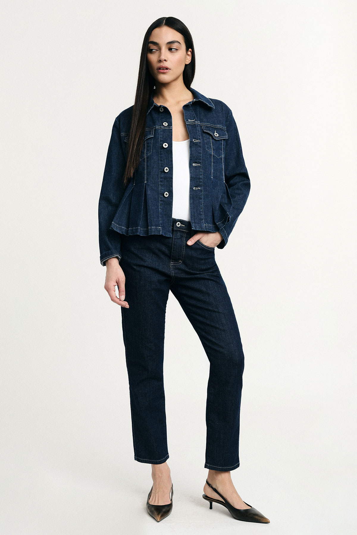 Woman modelling dark denim jacket and straight jeans, white top and black kitten heels, full-length on plain background
