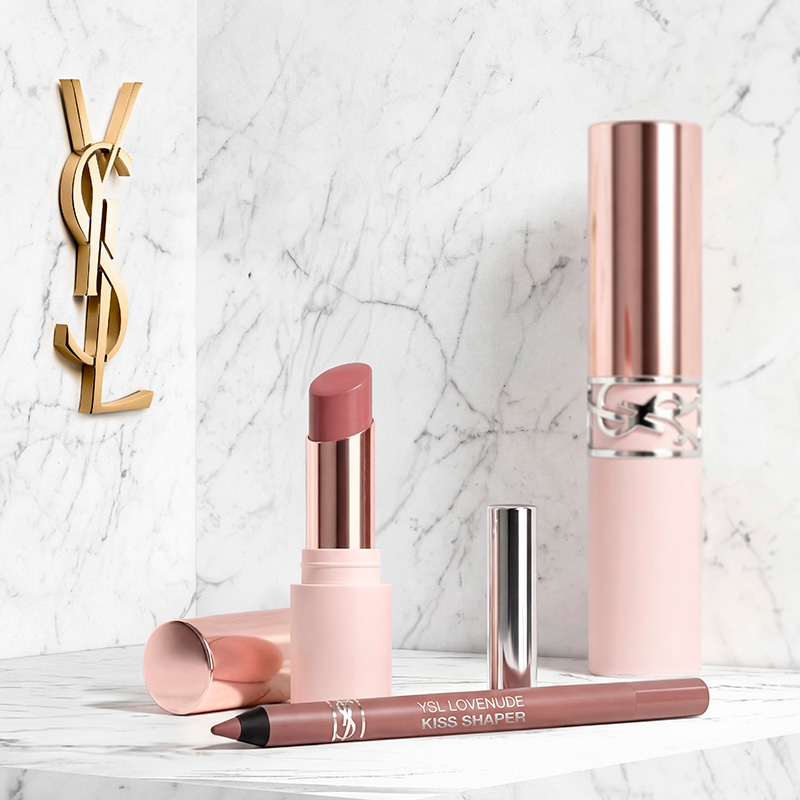 Prodotti per le labbra YSL in tonalit&agrave; rosa tenue su una superficie di marmo bianco con un logo dorato.