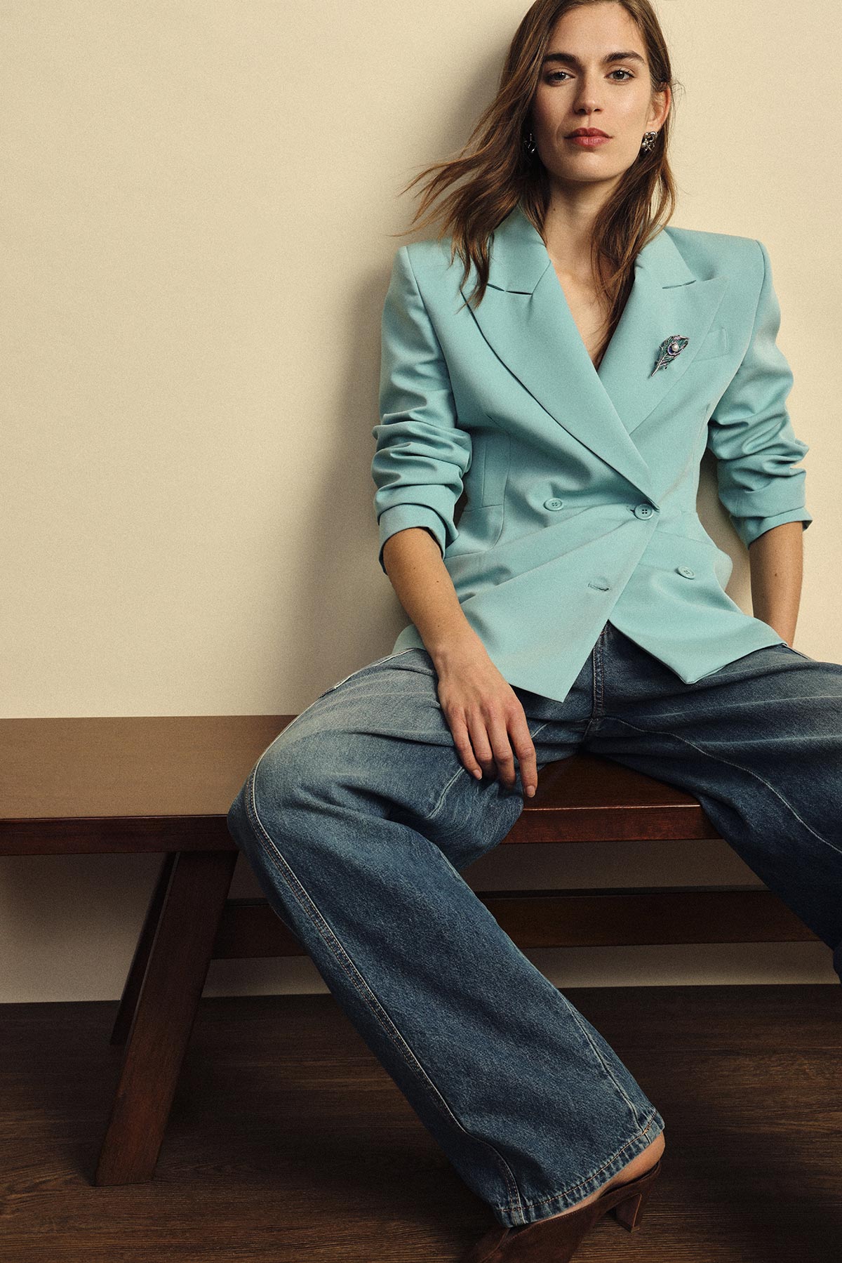 Woman in mint double-breasted blazer and wide-leg jeans seated on wooden bench, casual chic outfit