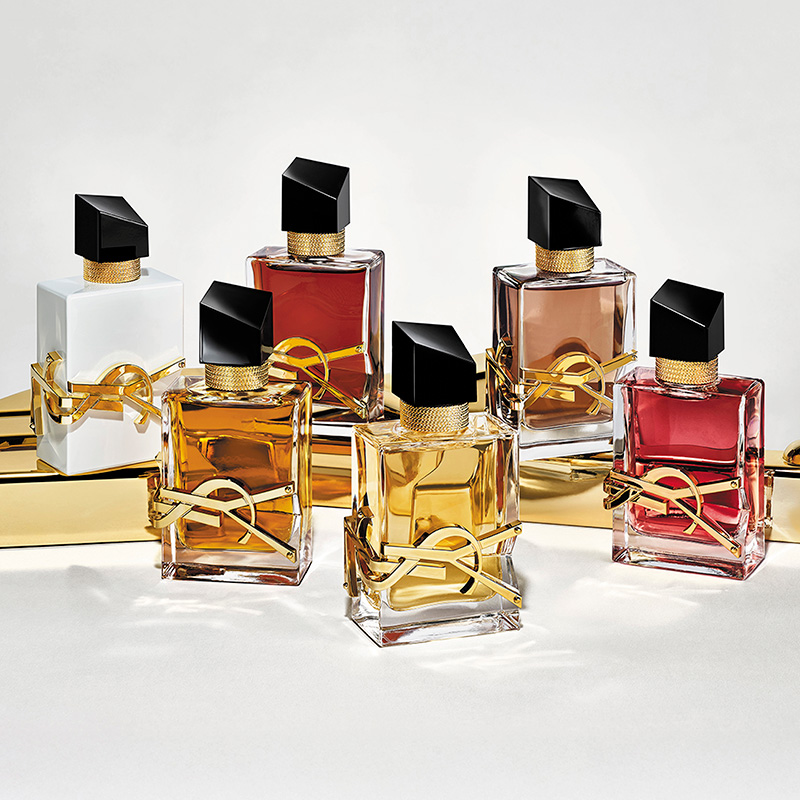 Una collezione di flaconi di profumo YSL Libre con liquidi colorati su una superficie di marmo e oro.