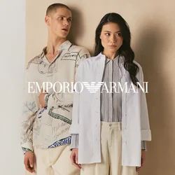 Due persone sono appoggiate a un pannello beige, una indossa una camicia a motivo e pantaloni color crema, l'altra un blazer bianco e pantaloni larghi color crema.