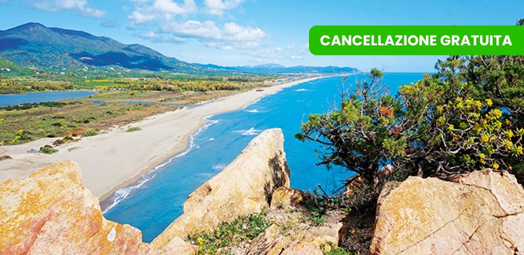 Turquoise sea, long sandy beach and rocky cliff with shrubs and distant mountains; green banner 'Cancellazione gratuita'