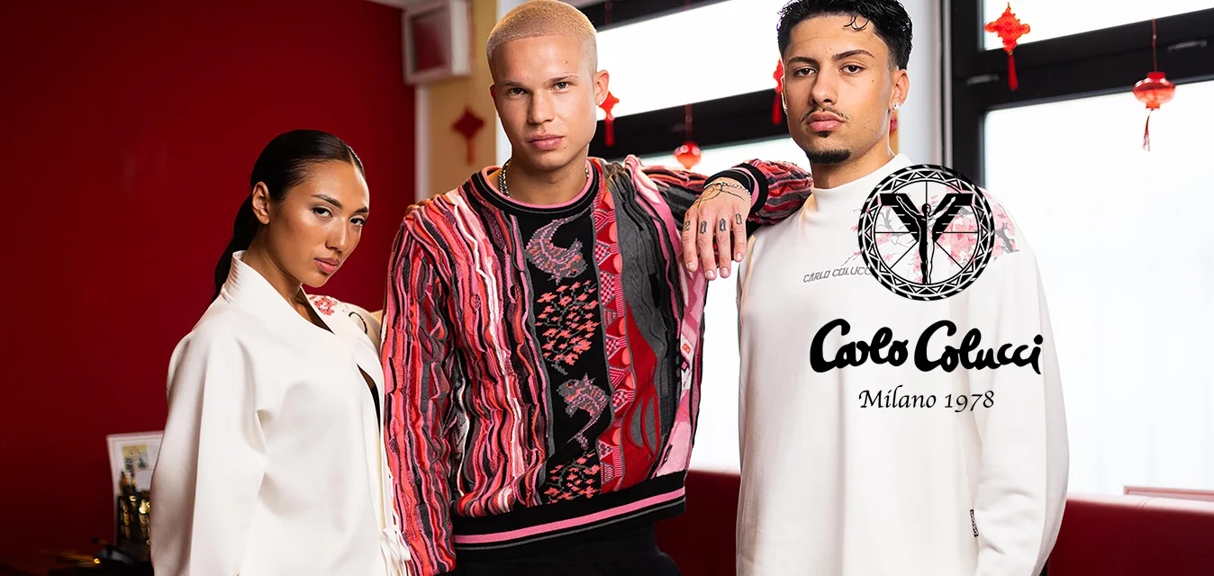 Tre persone posano all'interno indossando abiti eleganti e moderni in tonalità rosse e bianche, su uno sfondo di parete e finestra rossa.