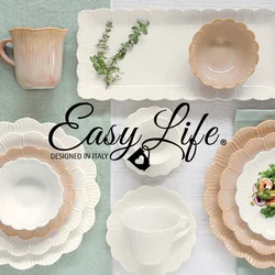 Piatti, ciotole e tazze in ceramica bianca e beige con bordi a scallop, disposti su sfondi verdi e bianchi, con un'insalata su un piatto e un rametto di verde.