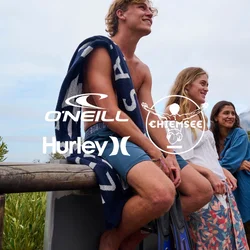 Tre persone sono sedute su un parapetto di legno, indossando abiti casual. Il paesaggio presenta vegetazione, colline rocciose e un cielo nuvoloso.