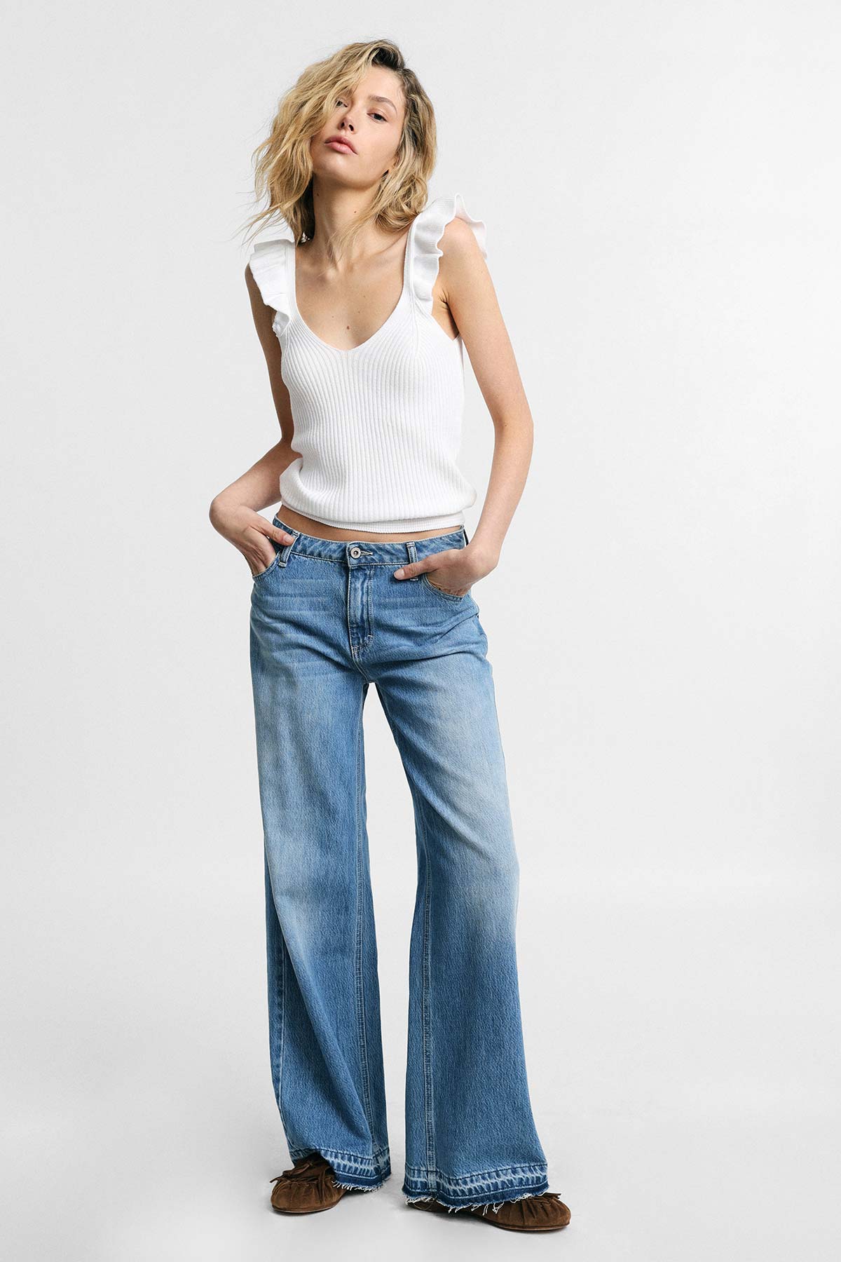 Woman wearing white ruffle sleeveless top and high-waist wide-leg blue jeans with brown moccasins