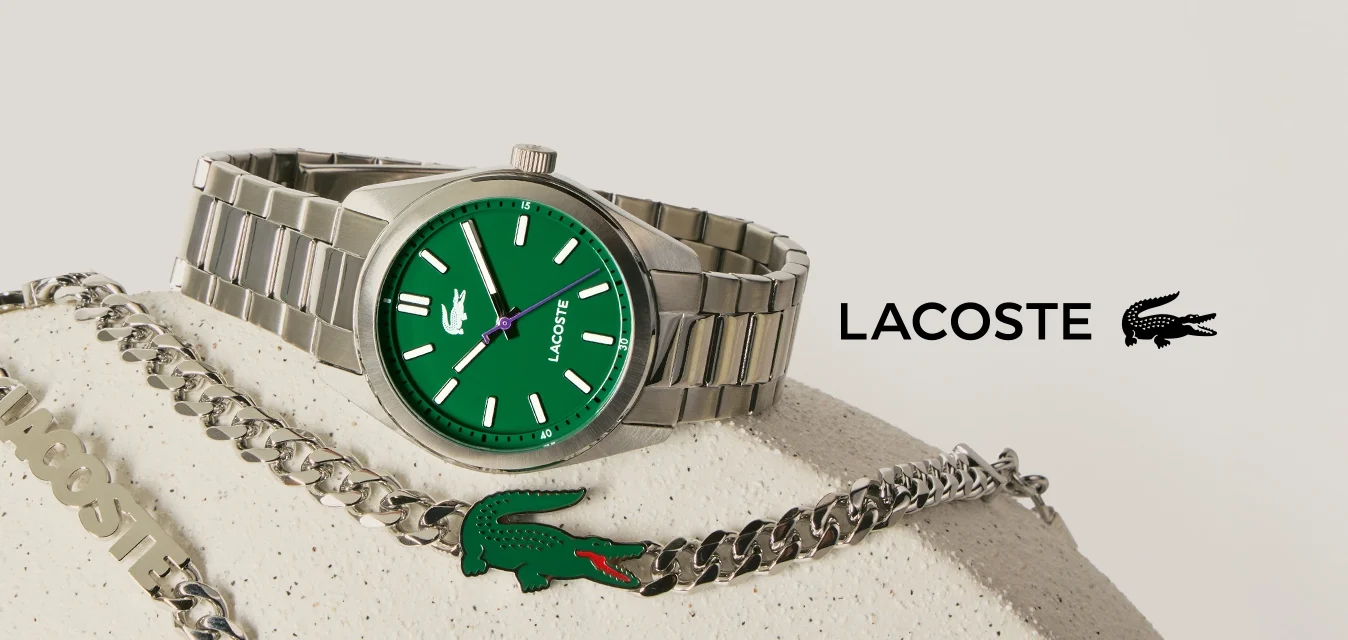 Orologio da polso d'argento con quadrante verde e collana a catena d'argento con emblema di coccodrillo verde su una superficie beige texturizzata.