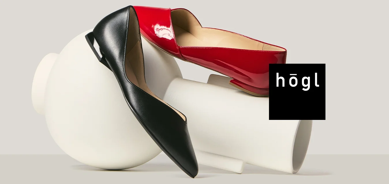 Due scarpe con tacchi alti, una rossa e una nera, posate su e attorno a forme astratte cilindriche e sferiche bianche.