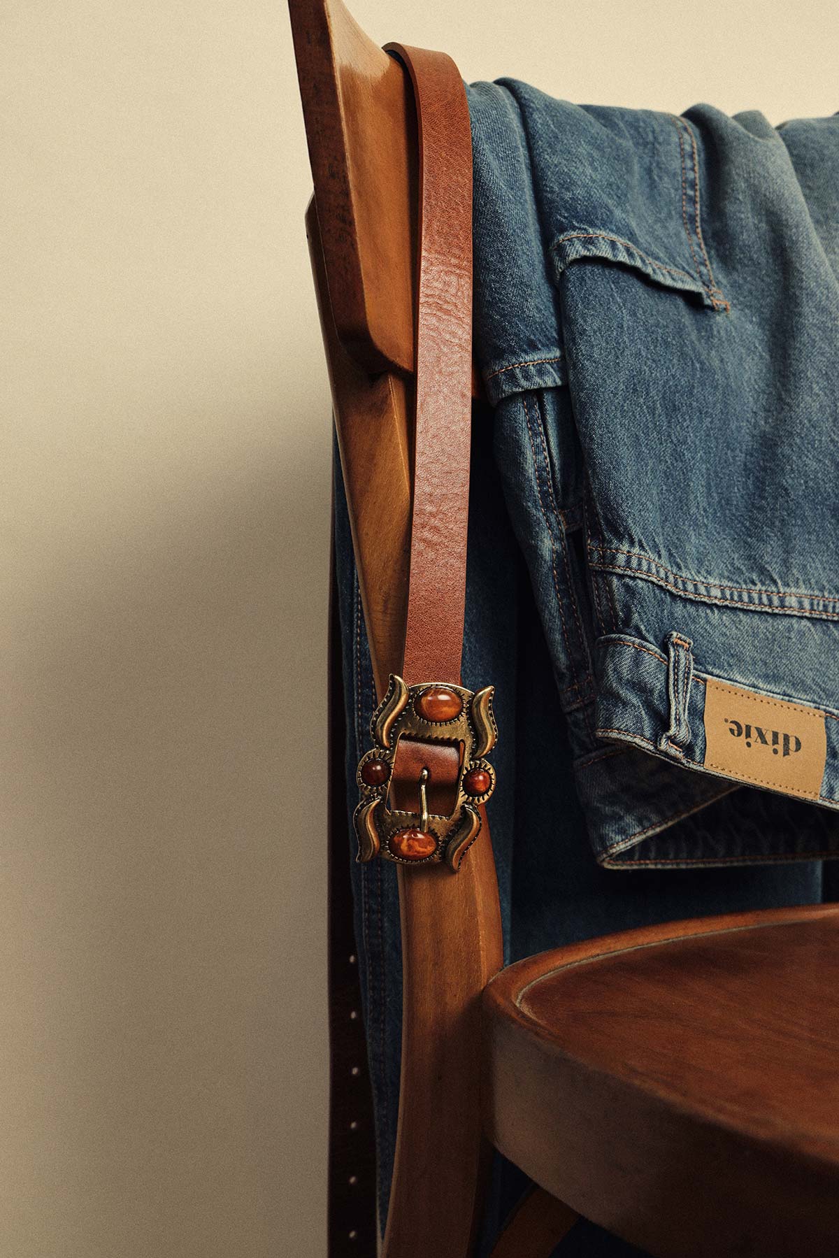 Brown leather belt with ornate brass buckle and folded blue denim jacket draped over a wooden chair
