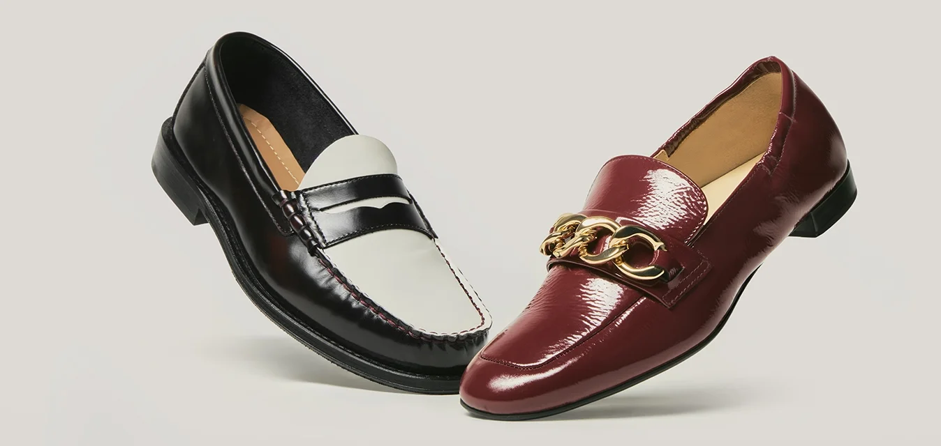 Due mocassini in pelle lucida: uno bianco e nero, l'altro rosso scuro con dettaglio a catena dorata, esposti su uno sfondo neutro.