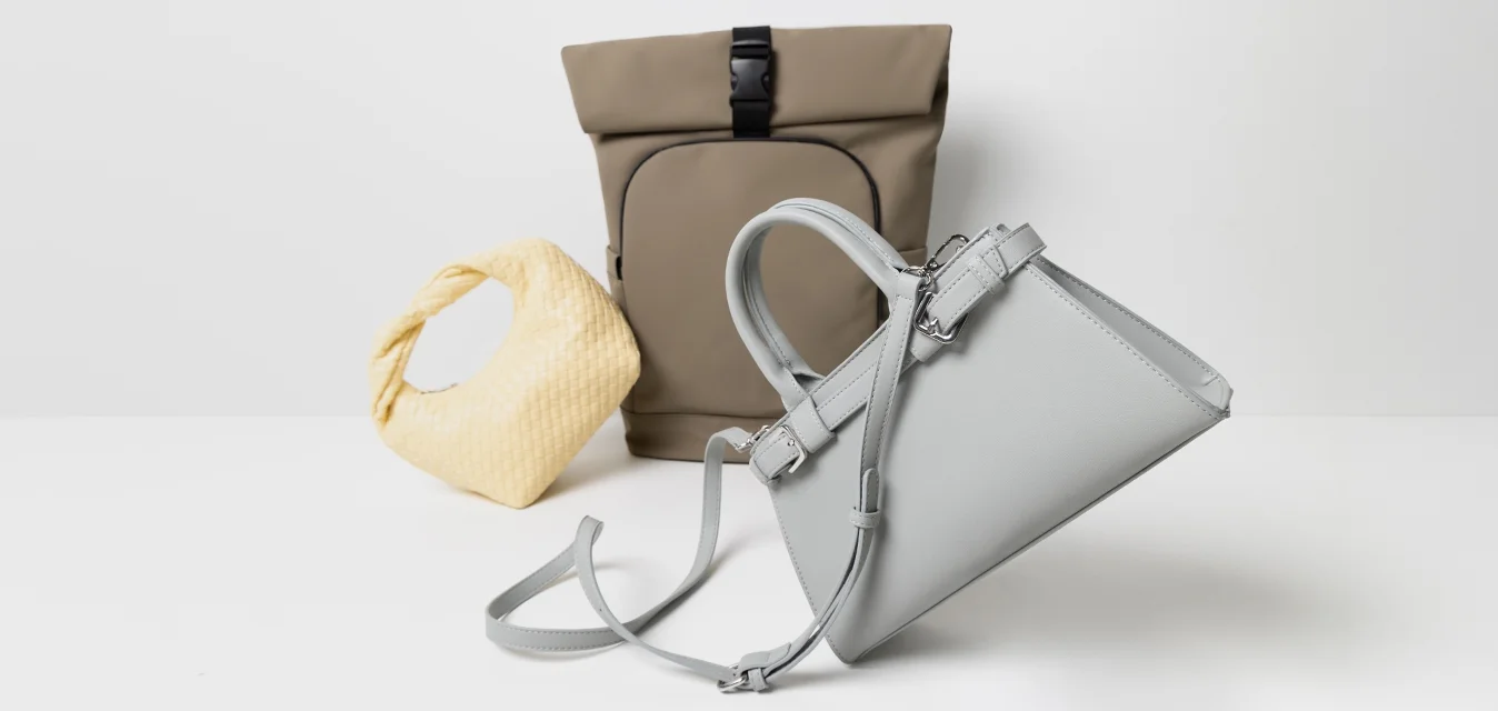 Tre borse: una borsa a tracolla grigia e angolare con un manico staccabile, una borsa hobo gialla in tessuto intrecciato, e uno zaino marrone con chiusura a rotolo e fibbia.