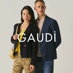 Donna con pantaloni a fantasia e blazer nero accanto a uomo con blazer blu e jeans su sfondo neutro.