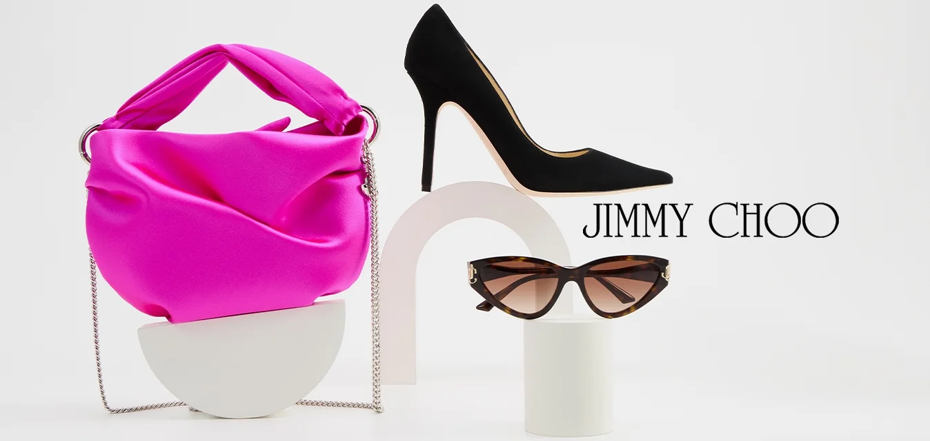 Borsa in satin rosa con manico annodato, décolleté nere a punta e occhiali da sole in acetato tartarugato esposti su stand bianchi astratti.