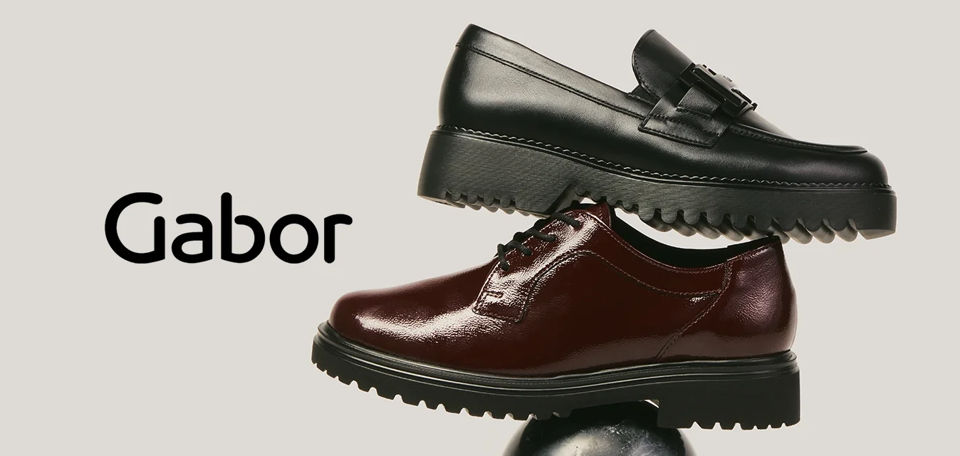 Mocassino in pelle nera impilato sopra una scarpa oxford marrone scuro lucida, entrambe bilanciate su una sfera di marmo nero contro uno sfondo semplice.