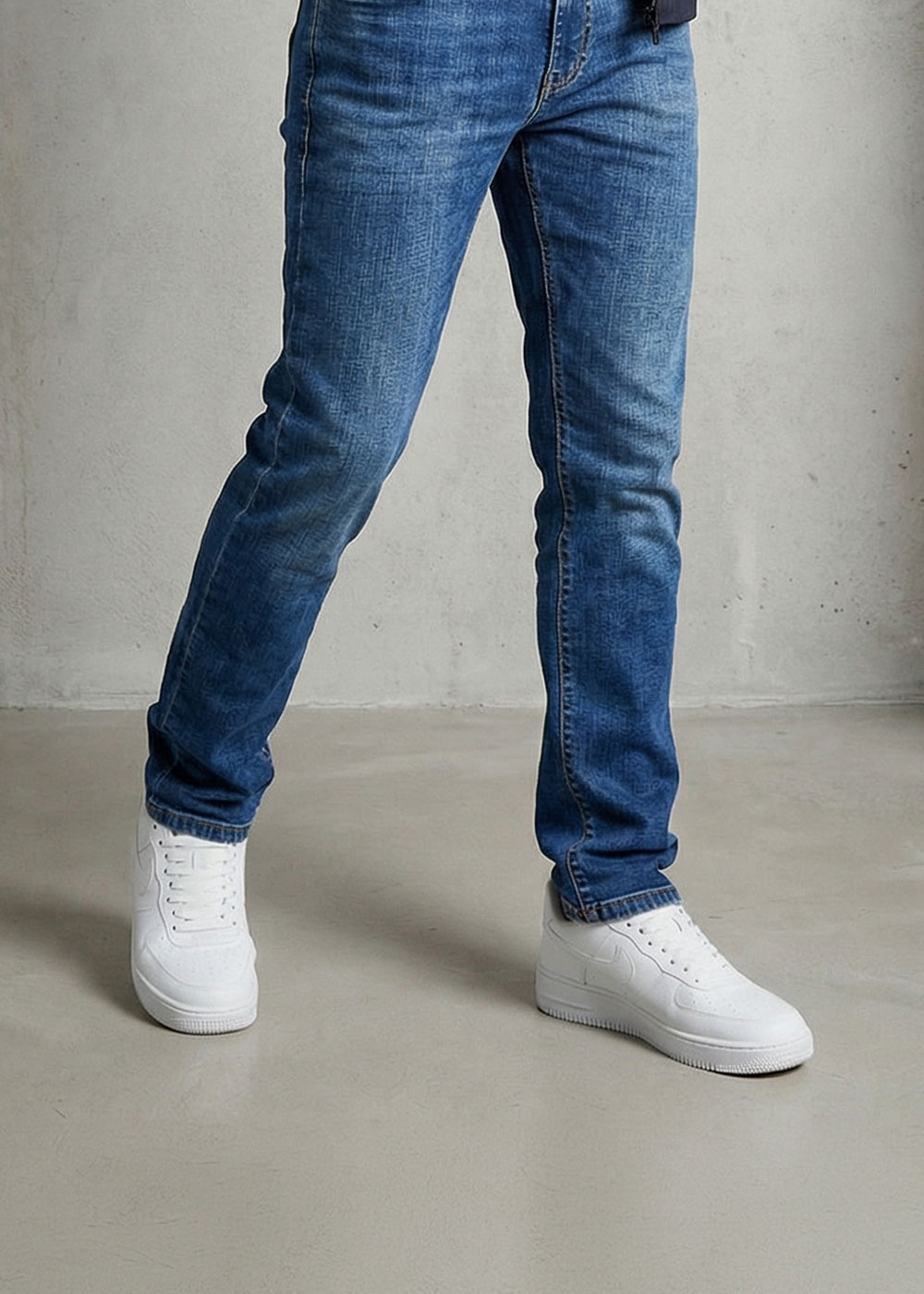 Legs wearing blue slim-fit jeans and white trainers on a concrete floor