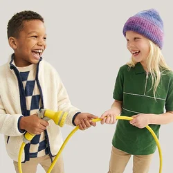 Due bambini, un ragazzo e una ragazza, sorridenti mentre tengono e giocano con un tubo da giardino giallo.