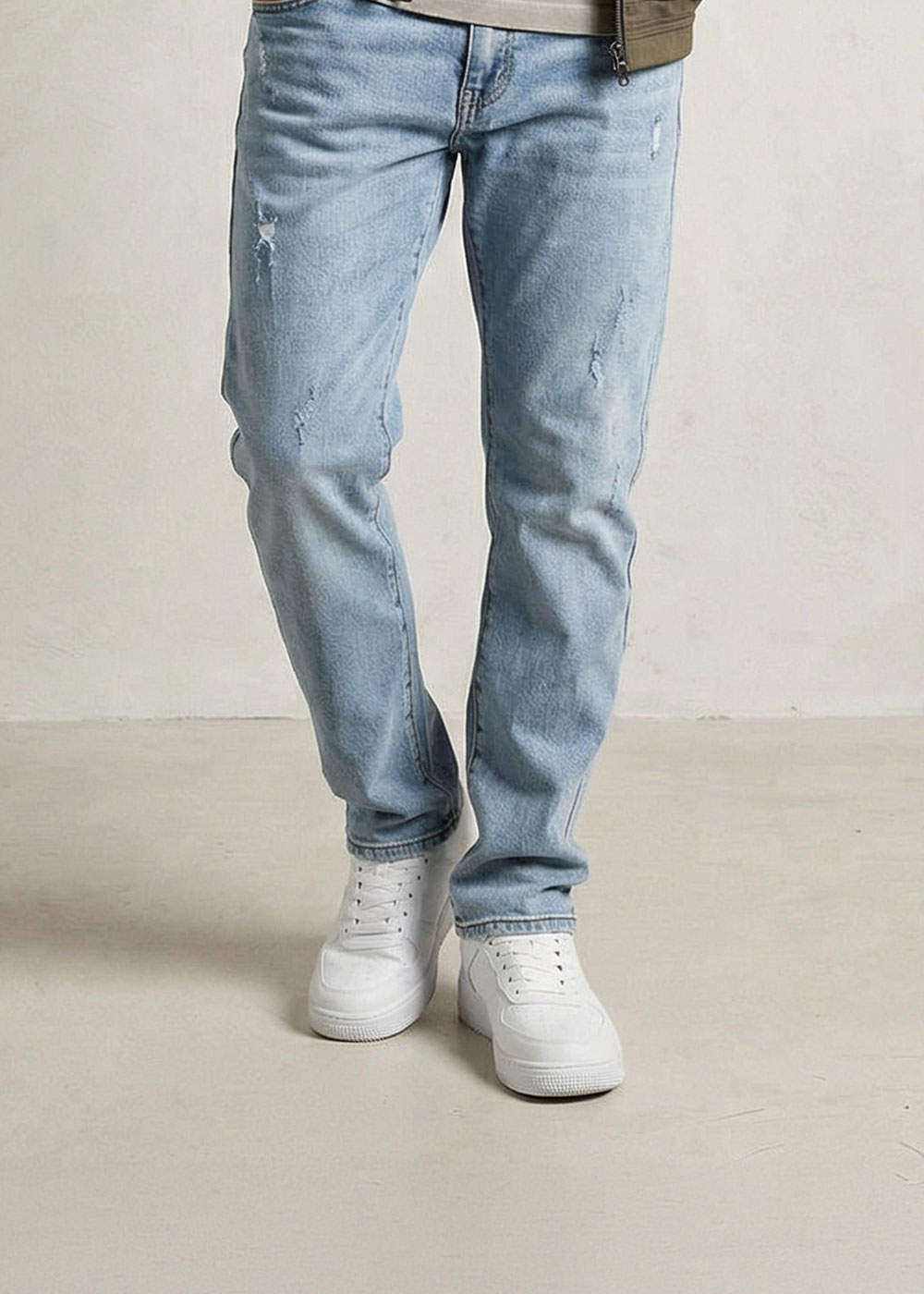 Lower body of person wearing light blue distressed slim-fit jeans and white trainers on a neutral background