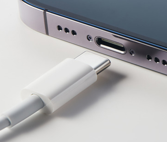 Primo piano della porta USB-C di uno smartphone con un cavo USB-C bianco pronto per essere collegato alla porta di ricarica dello smartphone.