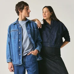 Uomo e donna in piedi uno di fronte all'altro, entrambi vestiti con abiti in denim scuro e scarpe nere, su uno sfondo grigio chiaro uniforme.