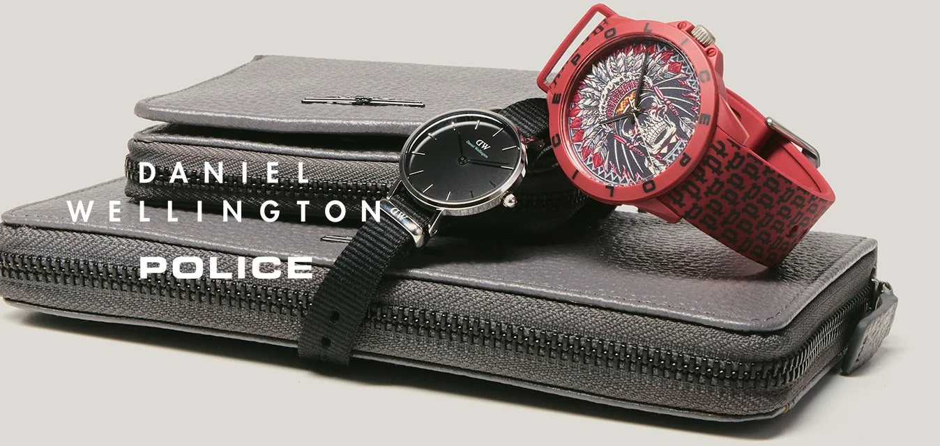 Due orologi da polso, uno nero con quadrante minimalista e uno rosso con quadrante decorativo, posizionati sopra due portafogli grigi con cerniera impilati uno sull'altro.