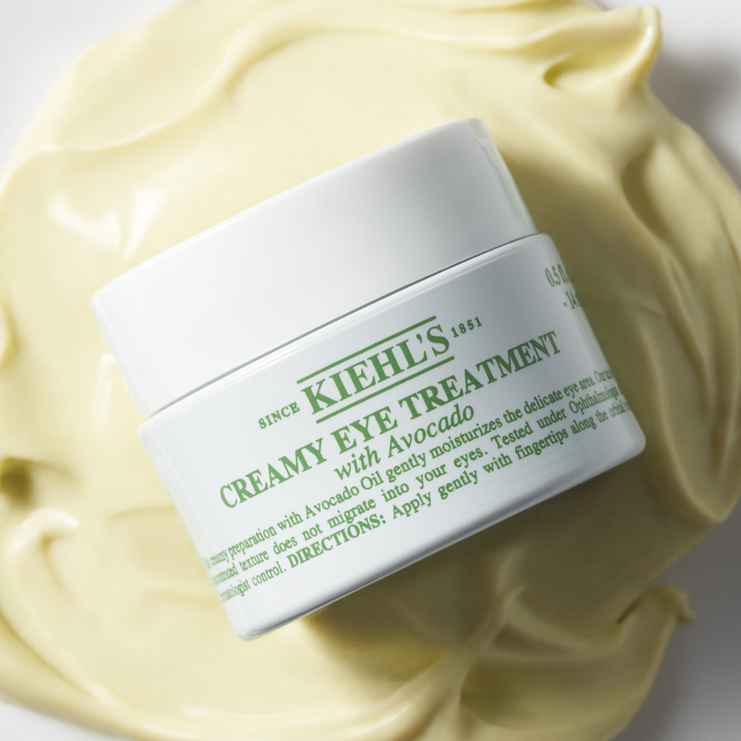 Vasetto di Creamy Eye Treatment with Avocado di Kiehl's immerso in una ricca texture di crema verde avocado