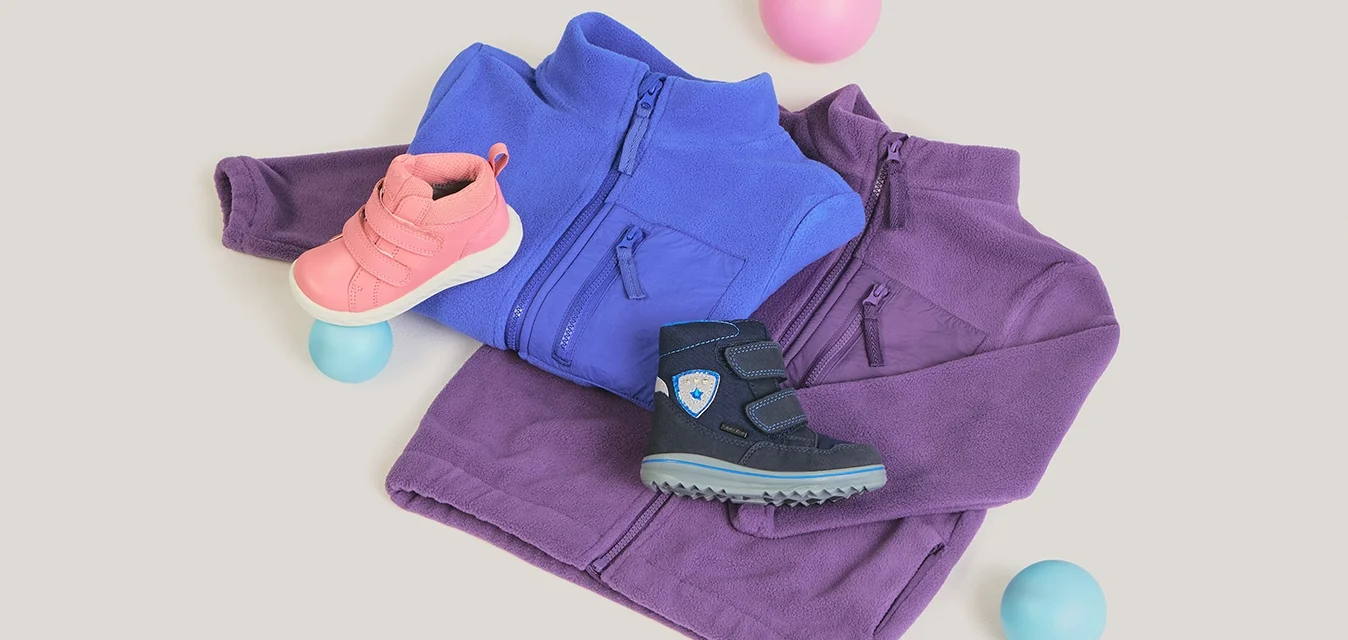 Due giacche in pile viola e blu, abbinate a scarpe per bambini rosa e nere, circondate da palline rosa e blu su sfondo bianco.