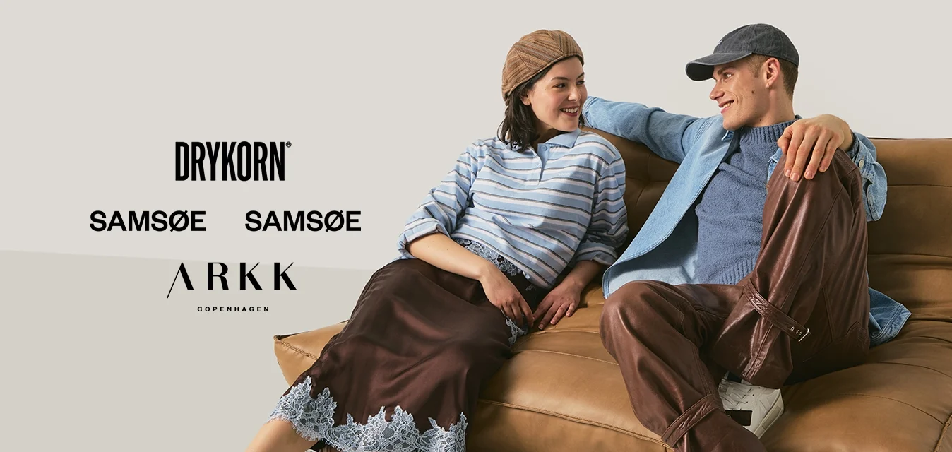 Due giovani adulti con abiti casual seduti e appoggiati su un divano marrone imbottito, sorridenti e che si guardano reciprocamente.