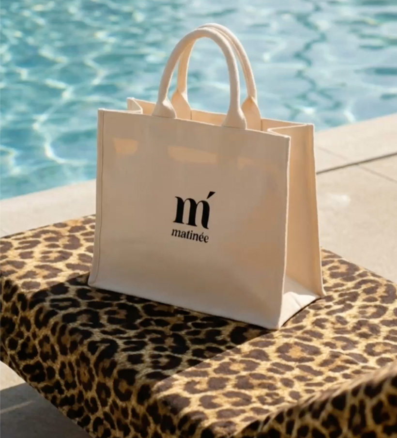 Cream canvas tote bag with "matinée" logo on a leopard-print towel beside a sunlit swimming pool
