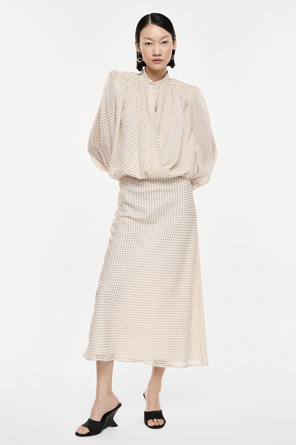 Woman modelling beige polka-dot blouse with puff sleeves and matching midi skirt, black mule heels, elegant women's outfit