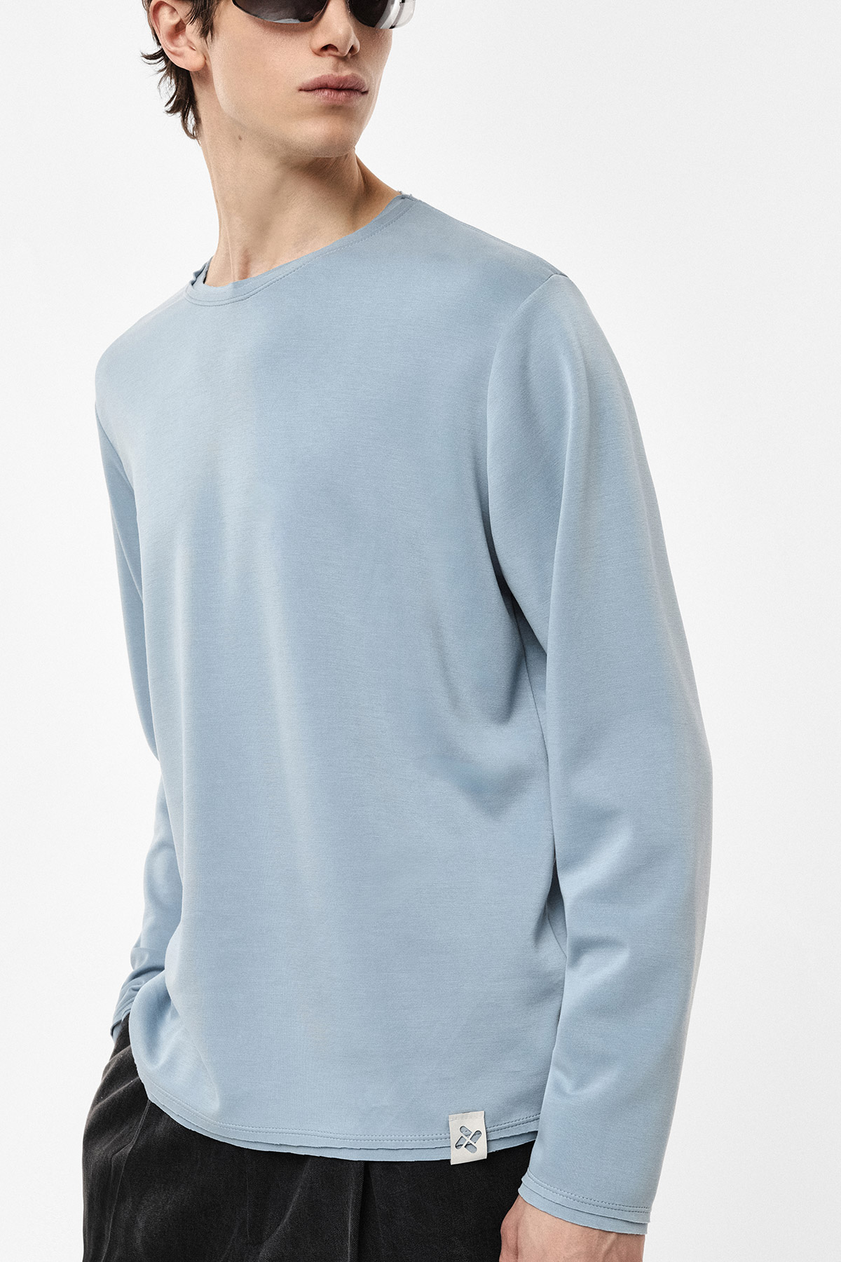 Man modelling light blue long-sleeve crew-neck top and black trousers in a relaxed side pose