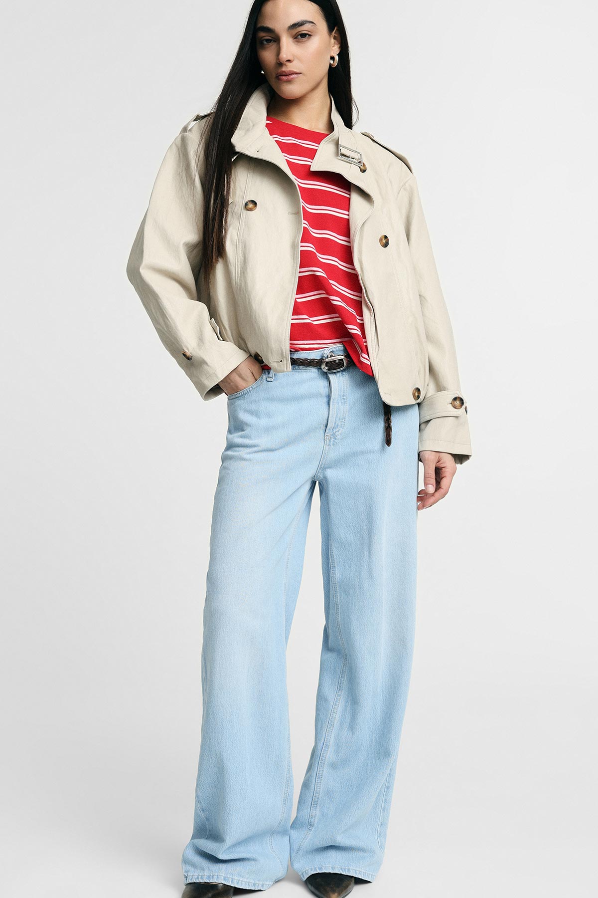 Woman modelling cropped beige trench jacket over red striped tee with light blue wide-leg jeans and brown belt